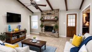 A living room with a fireplace, a ceiling fan, and a television. - Country Comfort - Spacious Brownwood Home (Early)