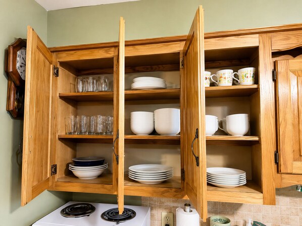A kitchen with wooden cabinets, a stove, and various dishes and glasses. - Country Comfort - Spacious Brownwood Home (Early)
