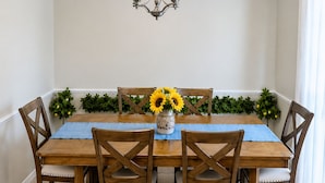 A dining room with a wooden table, chairs, a chandelier, and a vase with yellow flowers. - Country Comfort - Spacious Brownwood Home (Early)