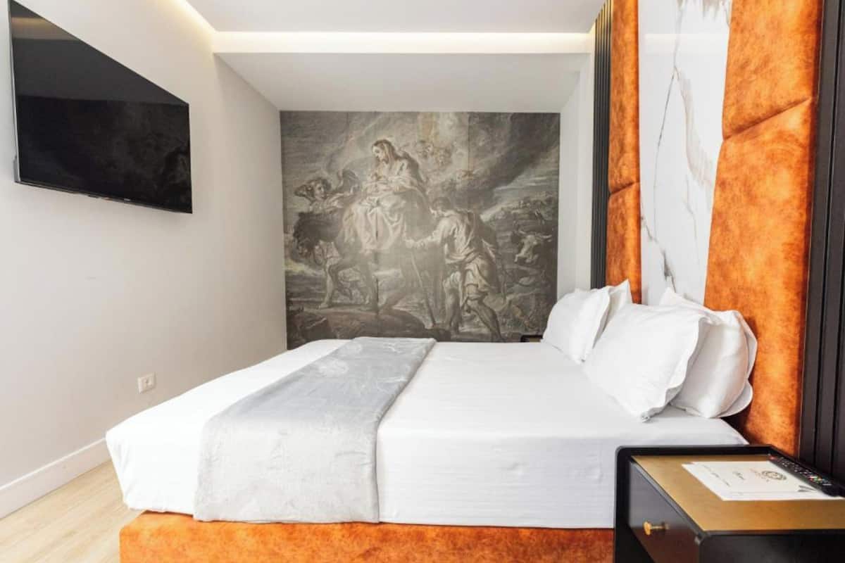 Una habitación de hotel moderna con una cama grande, un televisor de pantalla plana en la pared y un cabecero con diseño de mármol.