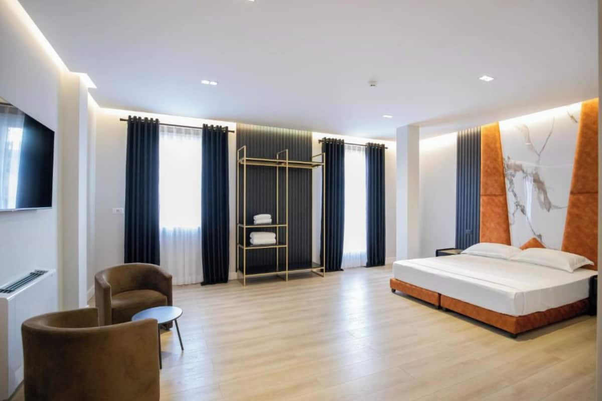 Una habitación de hotel moderna con una cama, una zona de estar con una silla y una mesita, un armario y un televisor montado en la pared.