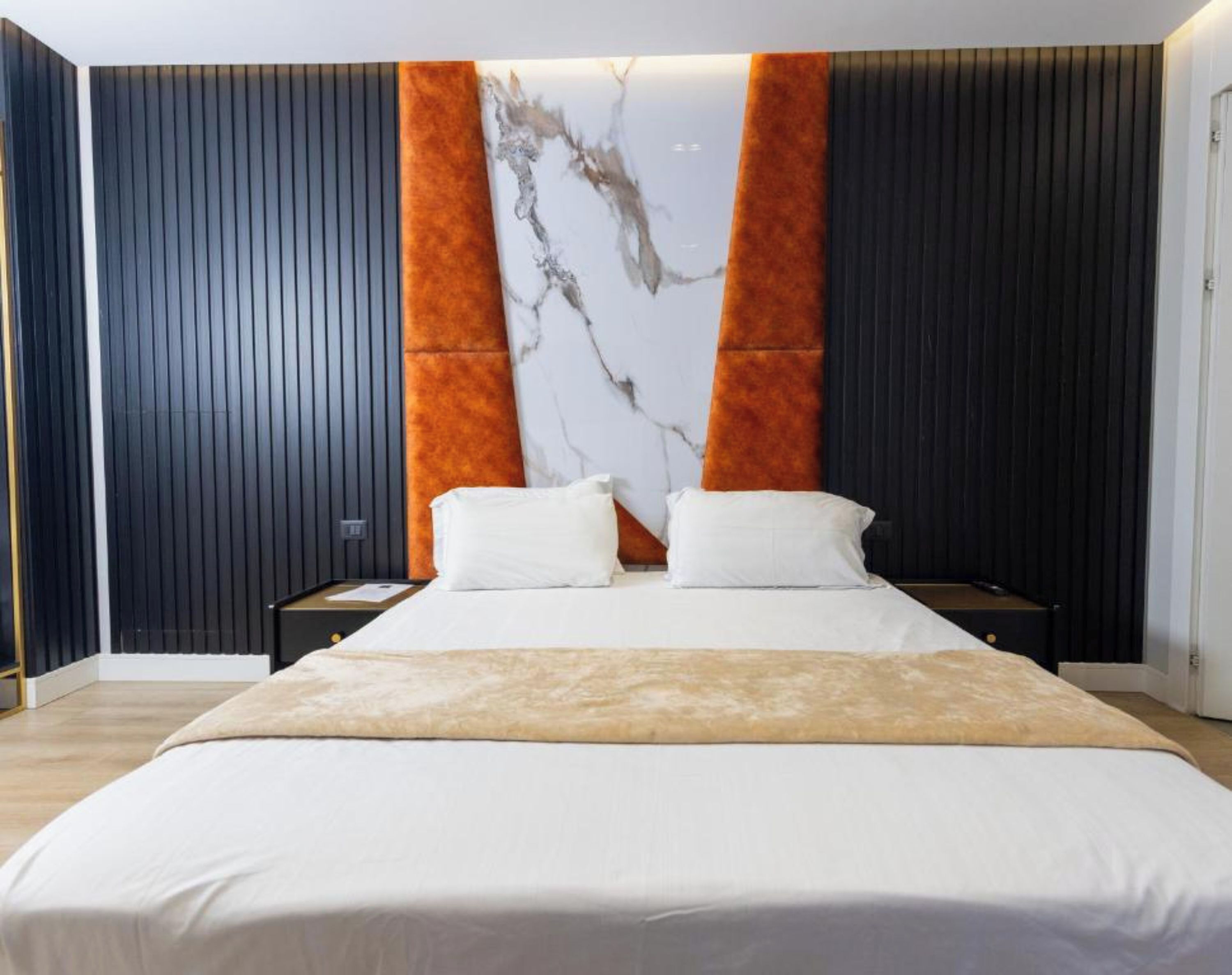 Un dormitorio moderno con una cama grande, dos mesitas de noche y una pared de acento de mármol.