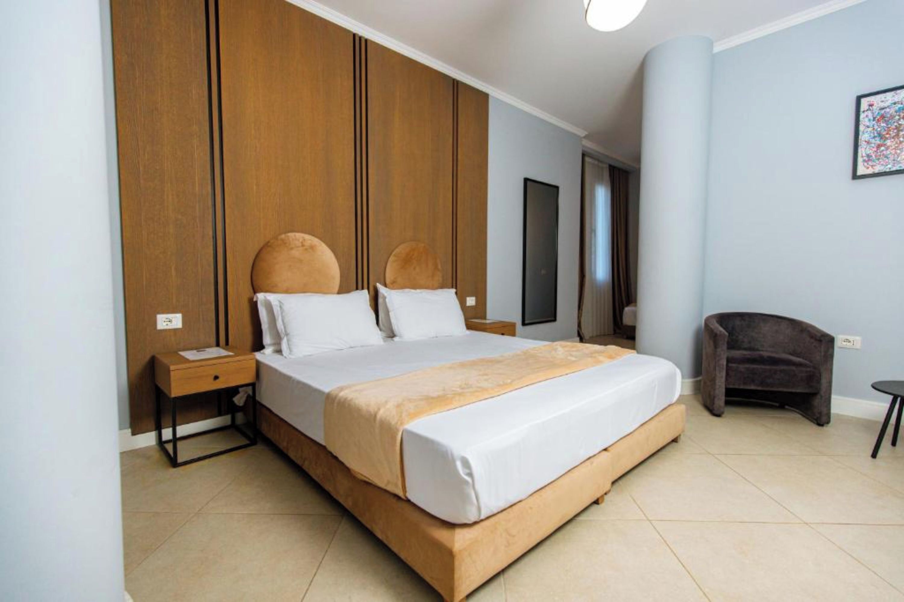 Ein Hotelzimmer mit einem großen Bett, Holzvertäfelung an den Wänden, einem kleinen Nachttisch, einem Sessel und einem gerahmten Bild.
