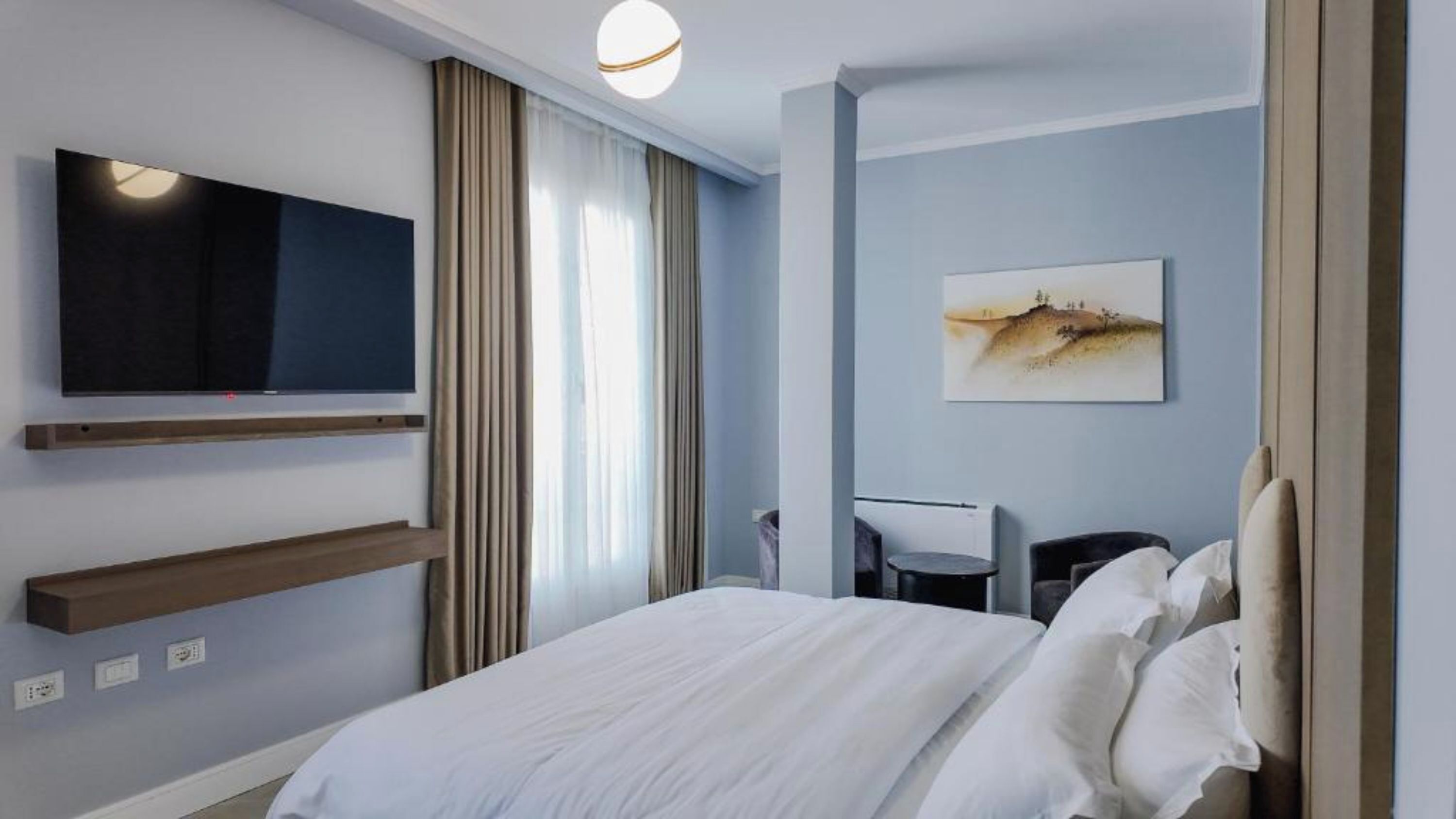 Une chambre d’hôtel moderne équipée d’un lit, d’un téléviseur fixé au mur, d’un bureau et d’un tableau décoratif.