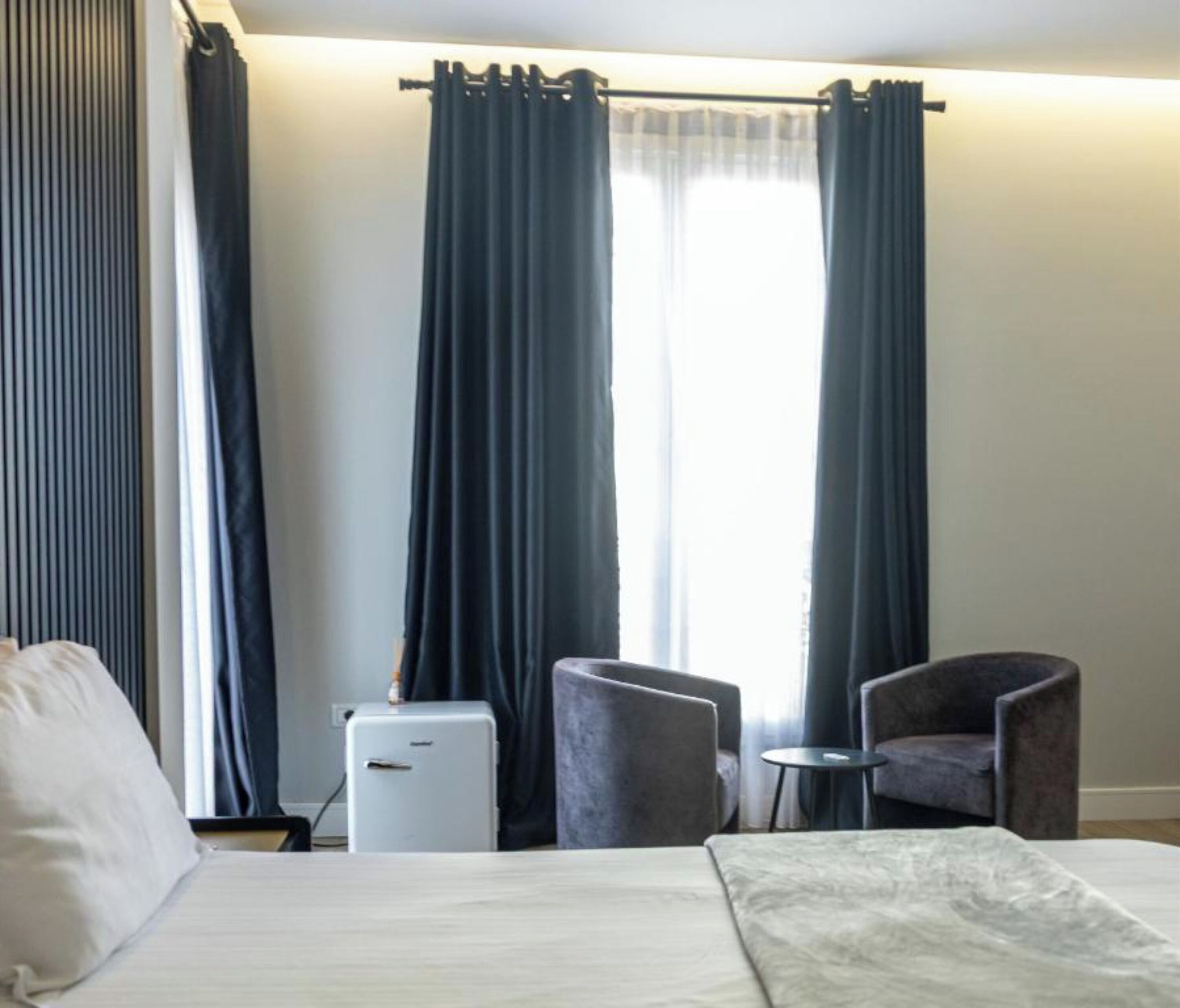 Habitación de hotel con una cama, una mesita, dos sillas y un refrigerador.