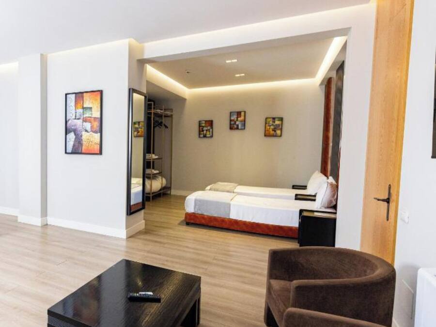 Una habitación de hotel moderna con una cama grande, una zona de estar con una mesa y obras de arte en las paredes.