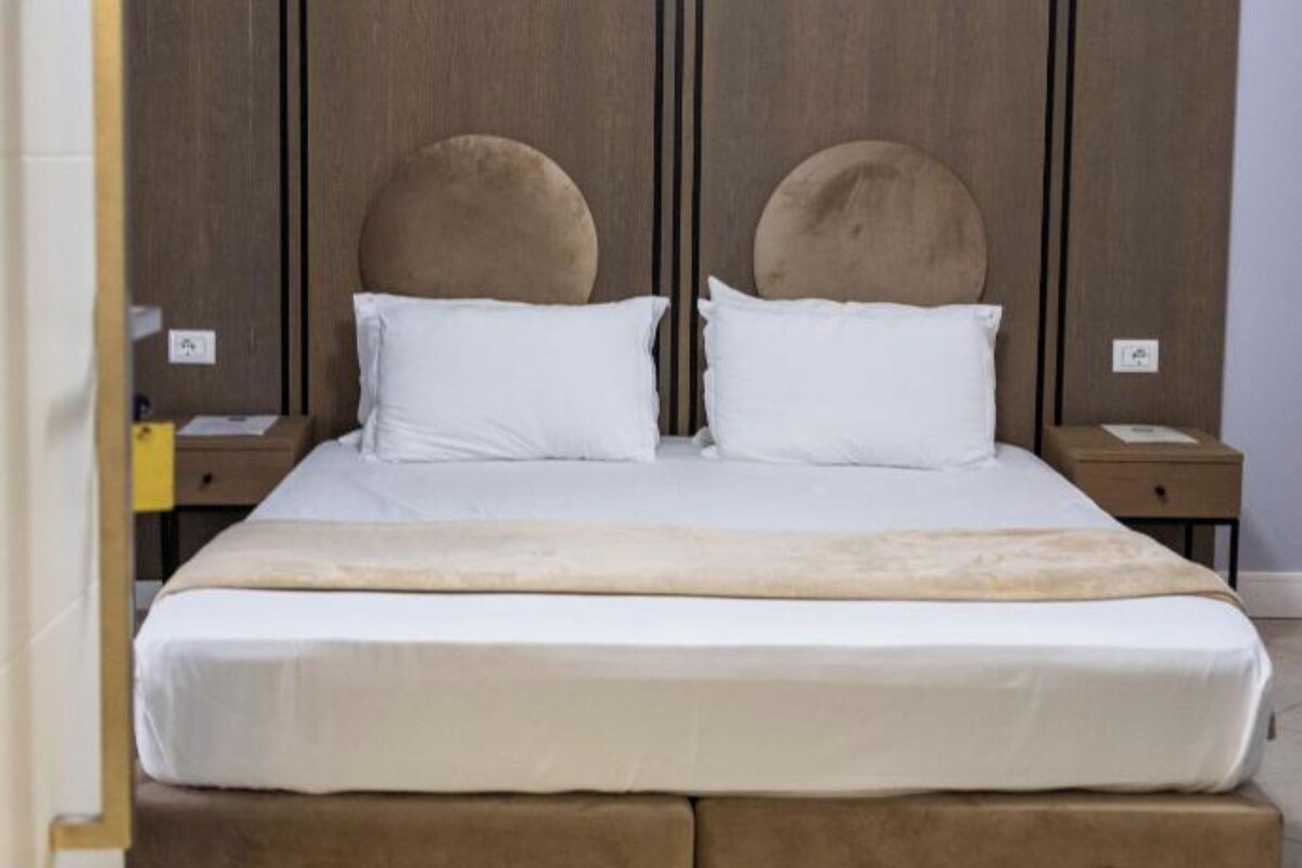 Un lit double avec une tête de lit et un pied de lit en bois, deux tables de chevet et une couvre-lit aux tons neutres.