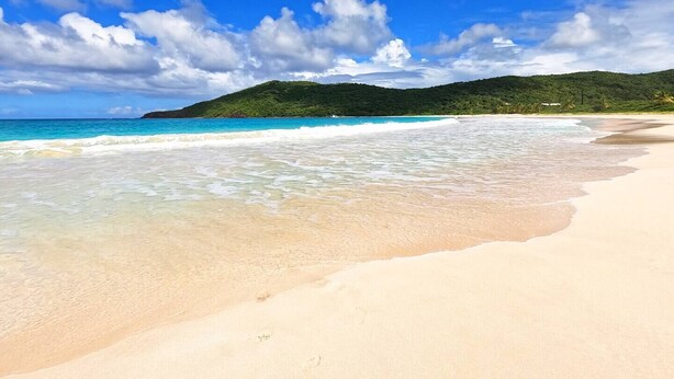 A beach with clear turquoise water, a sandy shore, and a green hill in the background. - Beautiful ocean view 4-bedroom house with AC in the island of Culebra PR (Culebra)