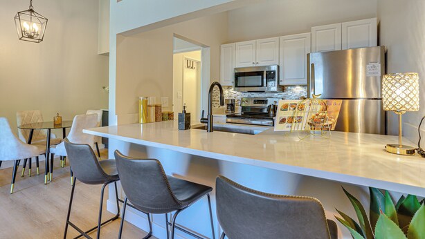 A modern kitchen with white cabinetry, stainless steel appliances, and a central island with bar stools.