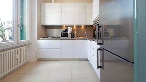 A modern kitchen with white cabinets, a stainless steel refrigerator, a microwave, and a gas stove. - 4BNB - Armot House Vatican Apartment (Rome)