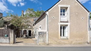 Un bâtiment à deux étages doté d’un balcon au deuxième étage, d’une cheminée bien visible et d’un petit jardin avec un arbre.