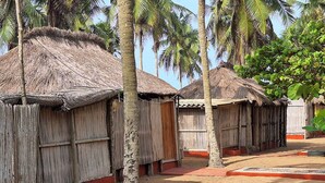 A row of thatched-roof huts with wooden walls and red trim, surrounded by palm trees. - cocobeach chez antoine avepozo (Lomé)
