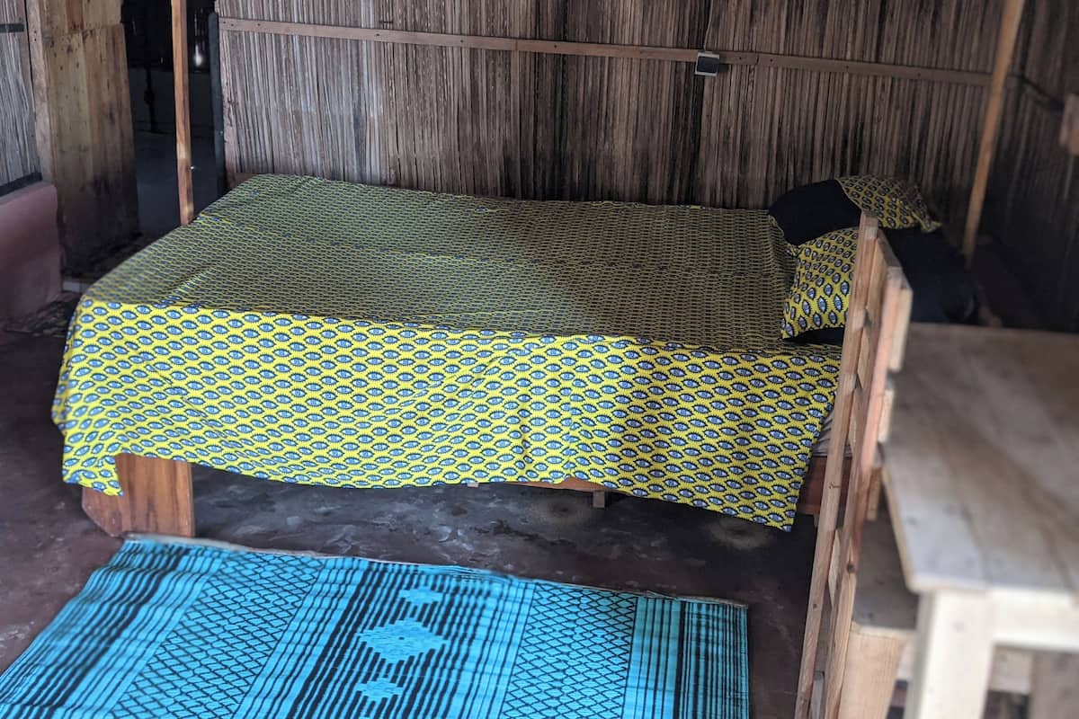 Un lit simple avec une couvre-lit à motifs, dans une chambre rustique aux murs en bois et au sol en béton.