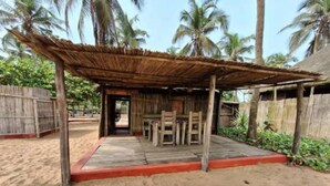 A rustic outdoor seating area with a thatched roof and wooden furniture, surrounded by sand and palm trees. - cocobeach chez antoine avepozo (Lomé)