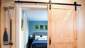 Une chambre avec une porte en bois, un lit, une table de chevet et une planche de paddle fixée au mur.