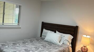A bedroom with a bed, a nightstand, a lamp, a window with blinds, and a ceiling light.