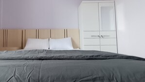 A bedroom with a bed, two pillows, a nightstand, and a white wardrobe.