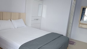 A neatly made bed with white bedding and a grey blanket, a wooden headboard, and a small bedside table with a lamp.