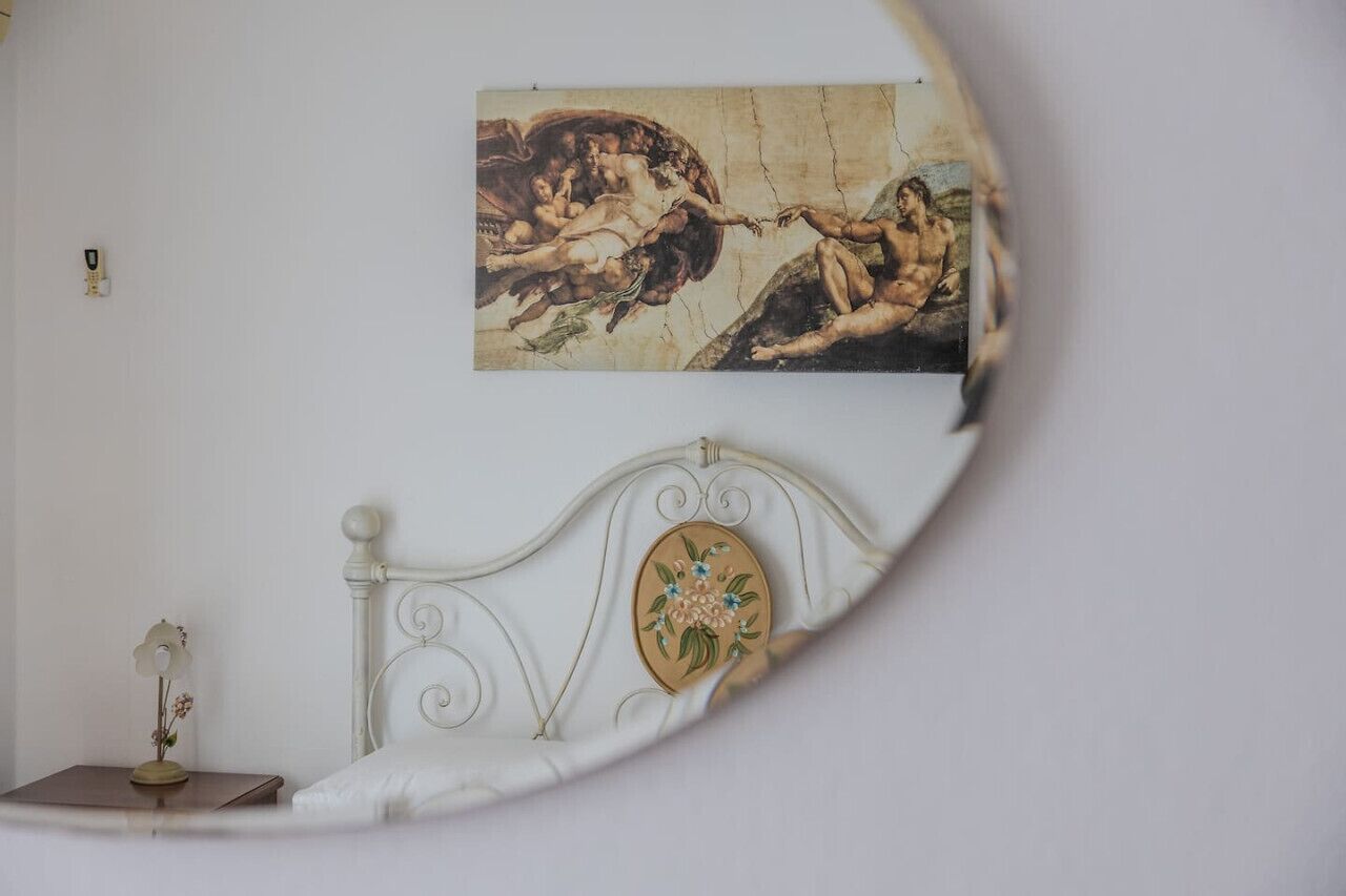 Een slaapkamer met een wit bed, een klein nachtkastje met een vaas en een schilderij aan de muur.