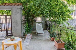 Un balcón con una silla blanca, una mesita con una planta y macetas.