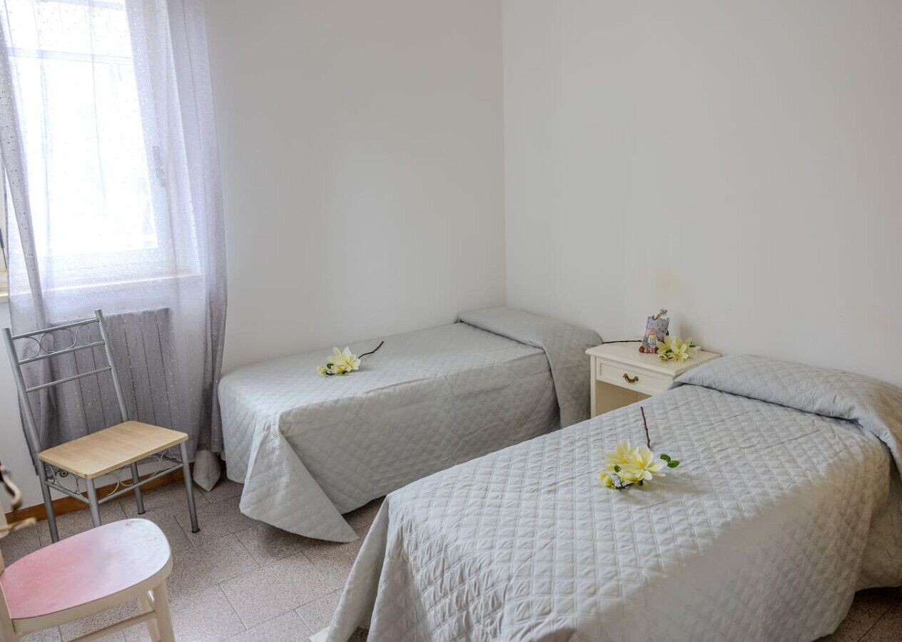 Una camera da letto con due letti, una sedia, un tavolino e una finestra con tende.
