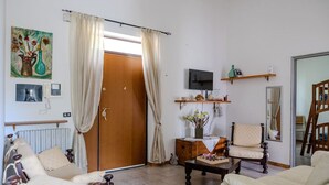 A living room with a wooden door, a television, a sofa, a chair, and a coffee table.