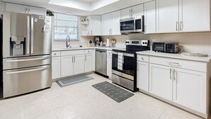 A modern kitchen with white cabinets, stainless steel appliances, a skylight, and a black countertop microwave.