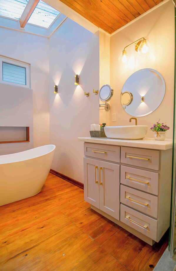 Un baño moderno con una bañera independiente, un tocador con lavabo y dos espejos montados en la pared.