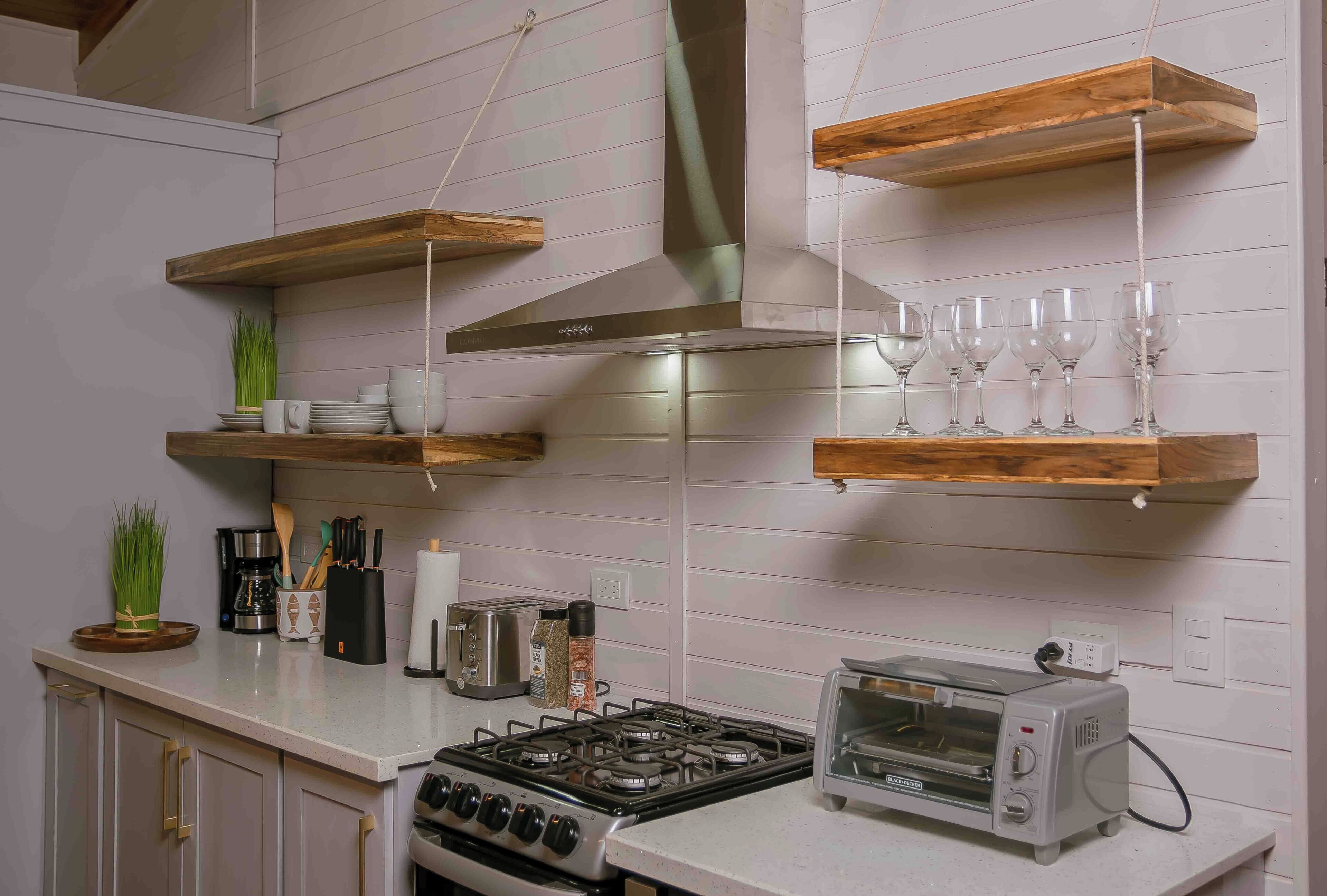 Una cocina con estantes de madera, estufa a gas, tostadora y diversos utensilios de cocina.