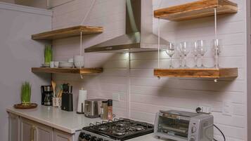 Una cocina con estantes de madera, estufa a gas, tostadora y diversos utensilios de cocina.