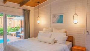 A bedroom with a large bed, wooden ceiling, and a view of an outdoor area with a pool and lounge chairs. - Cozy House with Pool+5min walk 2 beach-Near to west bay (Roatan)