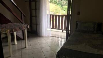 Quarto com cama, uma cadeira e escada que dá para uma varanda.