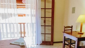A room with a bed, a table with a lamp, and a sliding door leading to an outdoor area. - POUSADA ANGRA BELLA (Angra dos Reis)