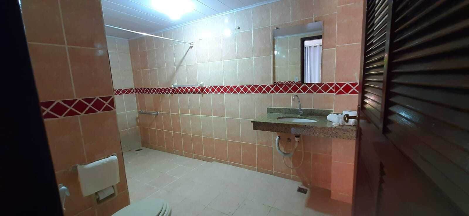 A bathroom with tiled walls, a sink, a mirror, and a shower area.