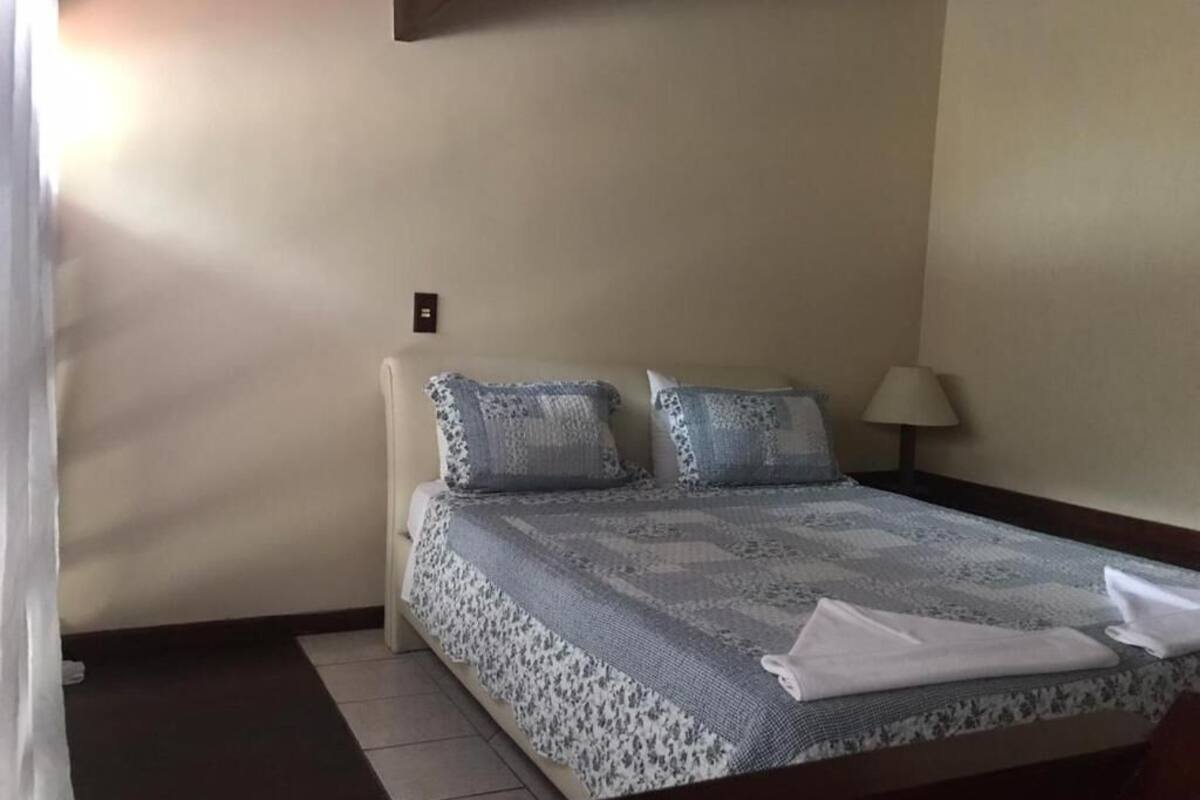 A neatly made bed with a floral-patterned bedspread and two matching pillows, a bedside lamp, and a folded towel on the bed.
