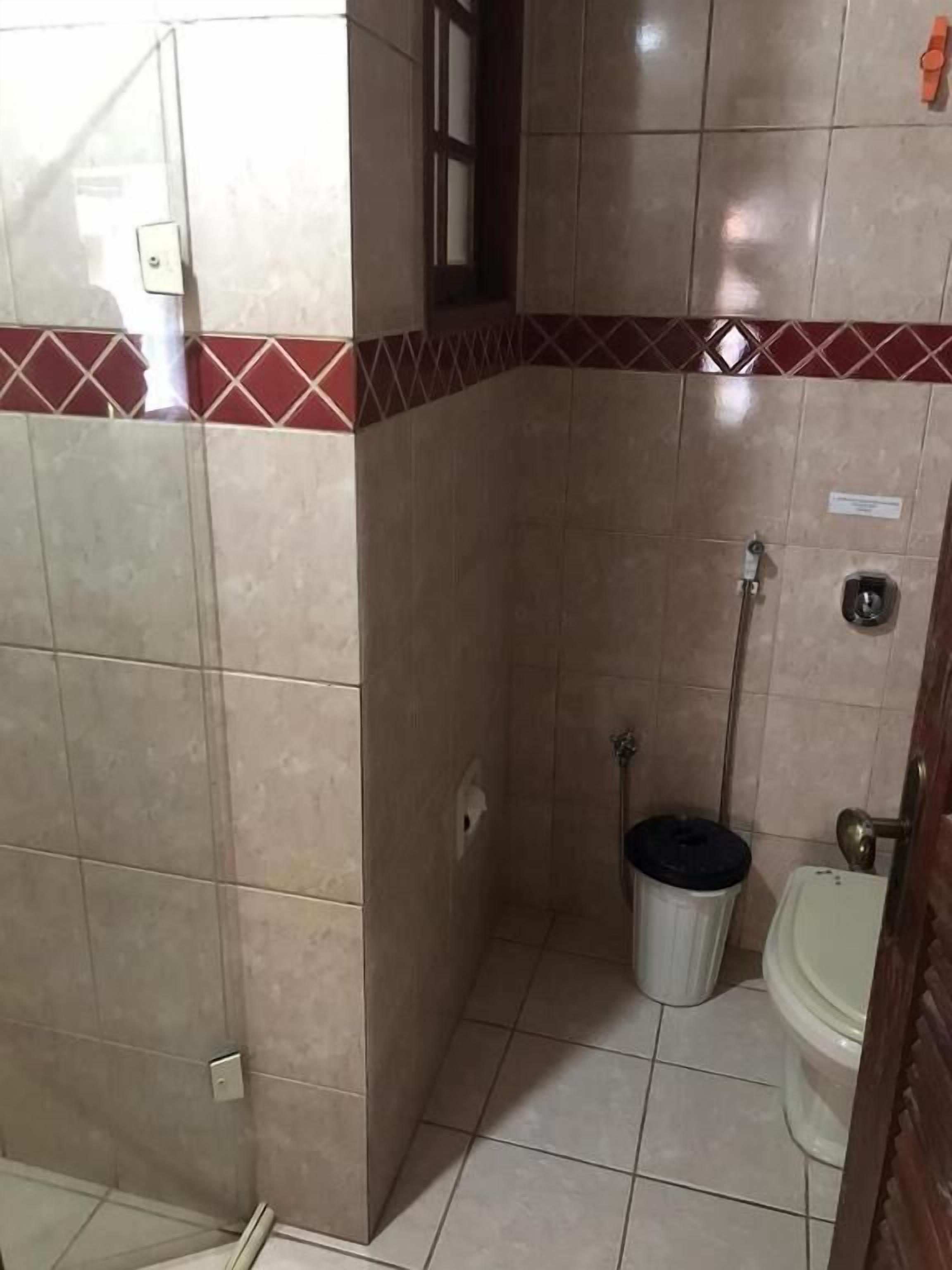 A small bathroom with a shower, toilet, and a trash bin.