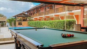 A pool table with balls, a brick fireplace, and a view of a building with balconies. - POUSADA ANGRA BELLA (Angra dos Reis)