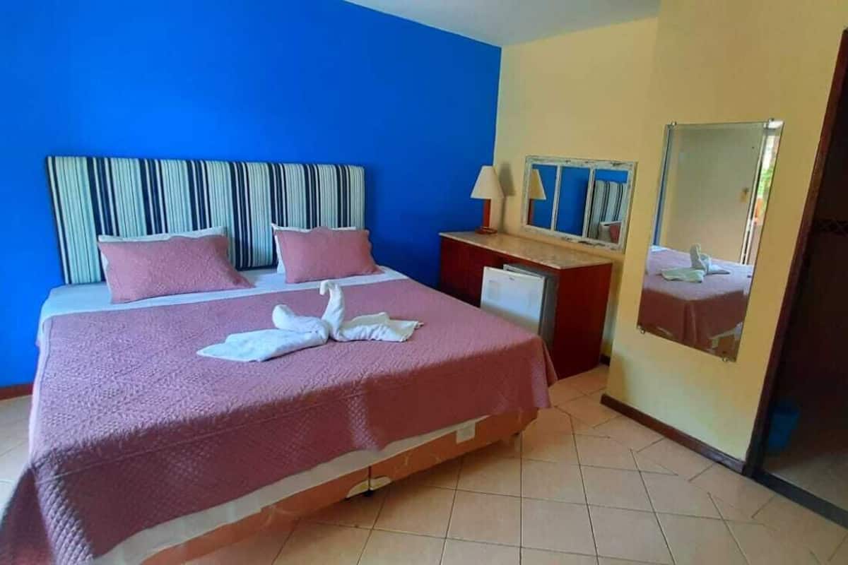 A hotel room with a large bed, a desk, a mirror, and a sliding door.