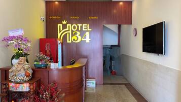 A hotel reception desk with a sign indicating it's Hotel 134, featuring a wooden reception area, a television mounted on the wall, and a decorative Buddha statue.