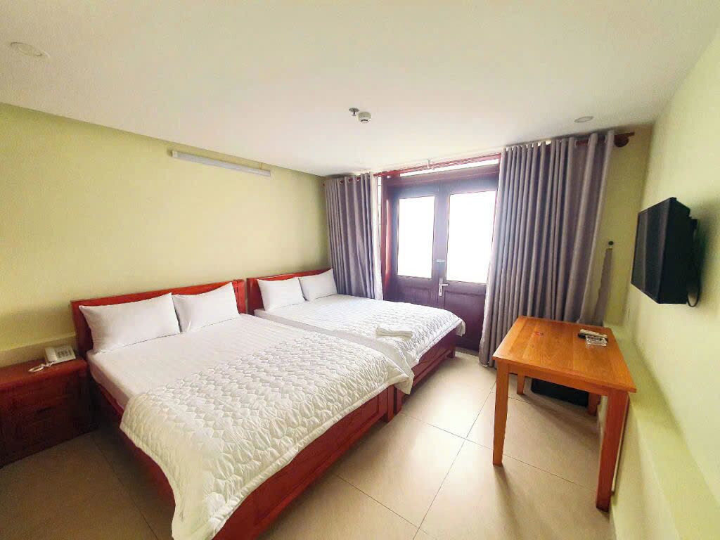 A hotel room with two beds, a wooden table, and a TV on the wall.