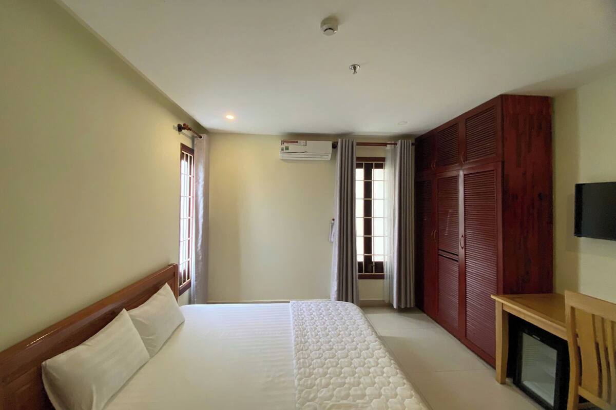 A bedroom with a bed, a wooden wardrobe, a television, and an air conditioning unit.