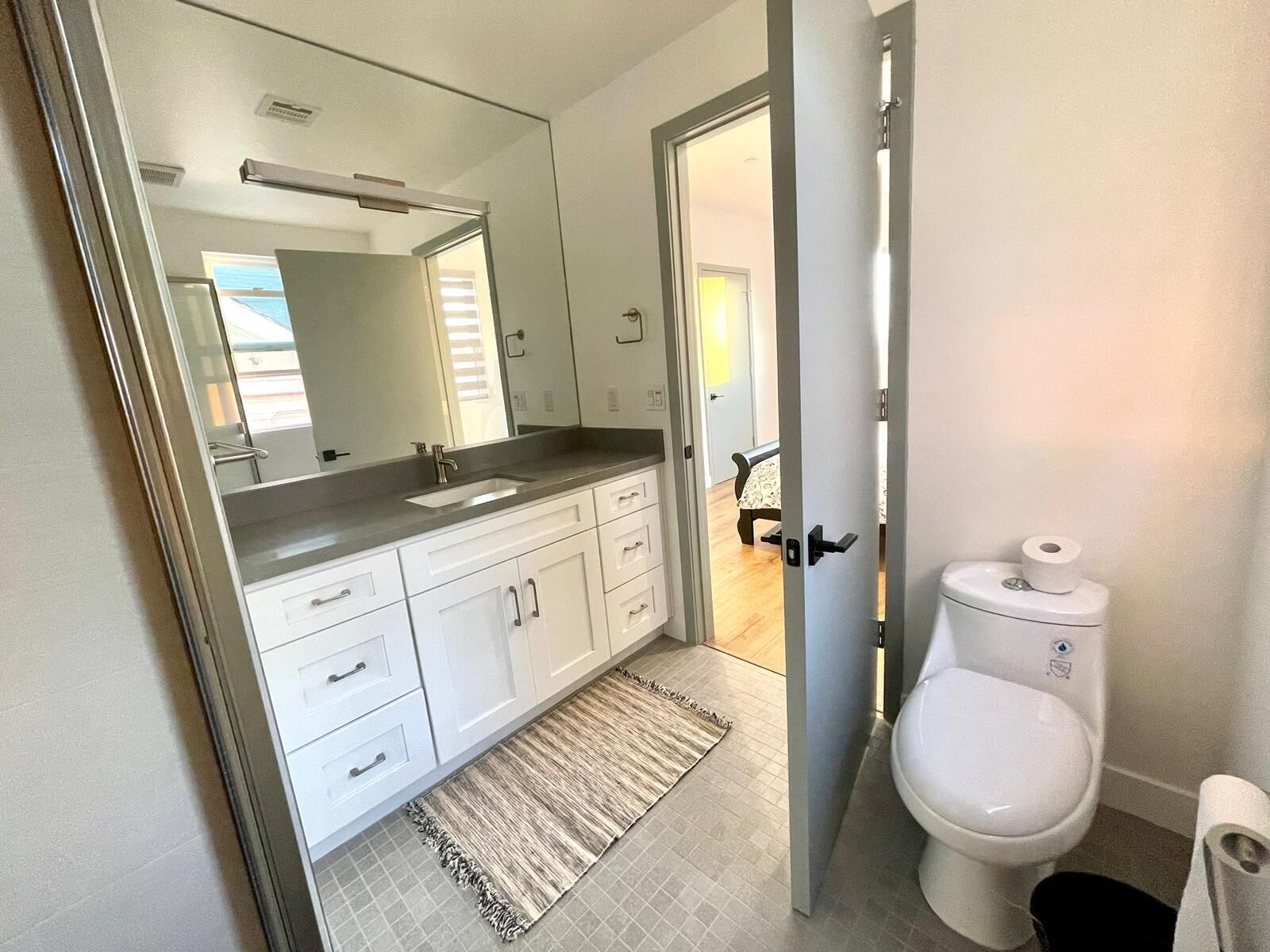 A modern bathroom with a sink, mirror, toilet, and a rug.