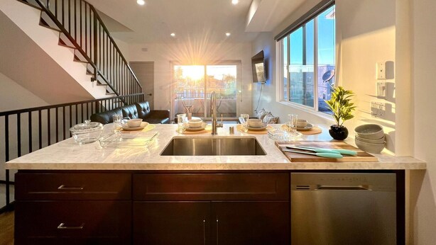 A modern kitchen with a central island, stainless steel appliances, and a view of the city through large windows.