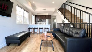 A modern living room with a black leather sofa, a wooden coffee table, and a kitchen in the background.