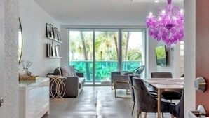 A modern living room with a dining area, large windows, and a view of greenery.