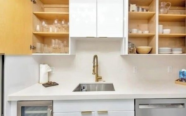 Une cuisine compacte avec des meubles blancs, un évier en acier inoxydable et un robinet doré.
