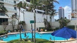 A swimming pool surrounded by palm trees and a building with multiple floors.