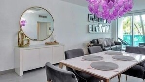 A modern living room with a white console, a round mirror, and a dining area with a white table and grey chairs.