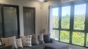 A modern living room with a sectional sofa, a round coffee table, and large windows offering a view of greenery. - MetzManor:Modern luxury Kgn retreat, scenic views,balconies,gated,self check-in  (Kingston)
