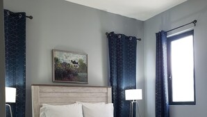 A bedroom with a wooden bed, a nightstand, a lamp, a painting, and a window with curtains. - MetzManor:Modern luxury Kgn retreat, scenic views,balconies,gated,self check-in  (Kingston)